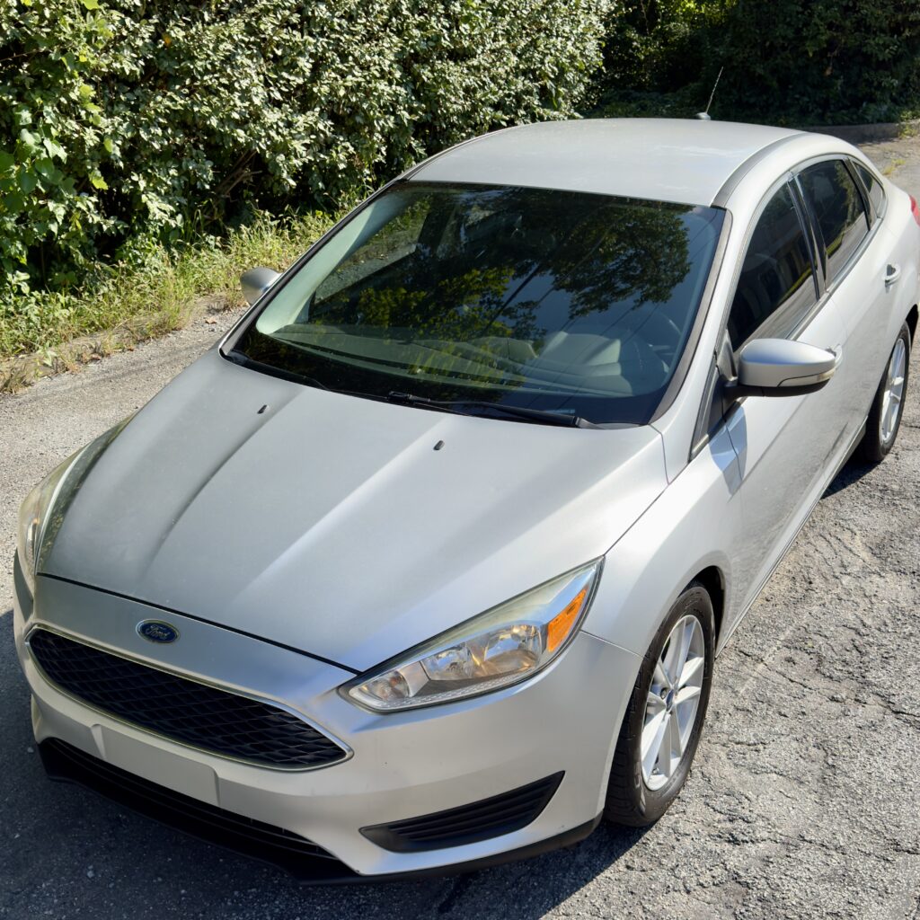 2016 Ford focus in sleek silver, captured from a high-angle view. This compact sedan showcases its aerodynamic design, clear headlights, and smooth body lines, making it a perfect blend of style and efficiency for your daily drives.